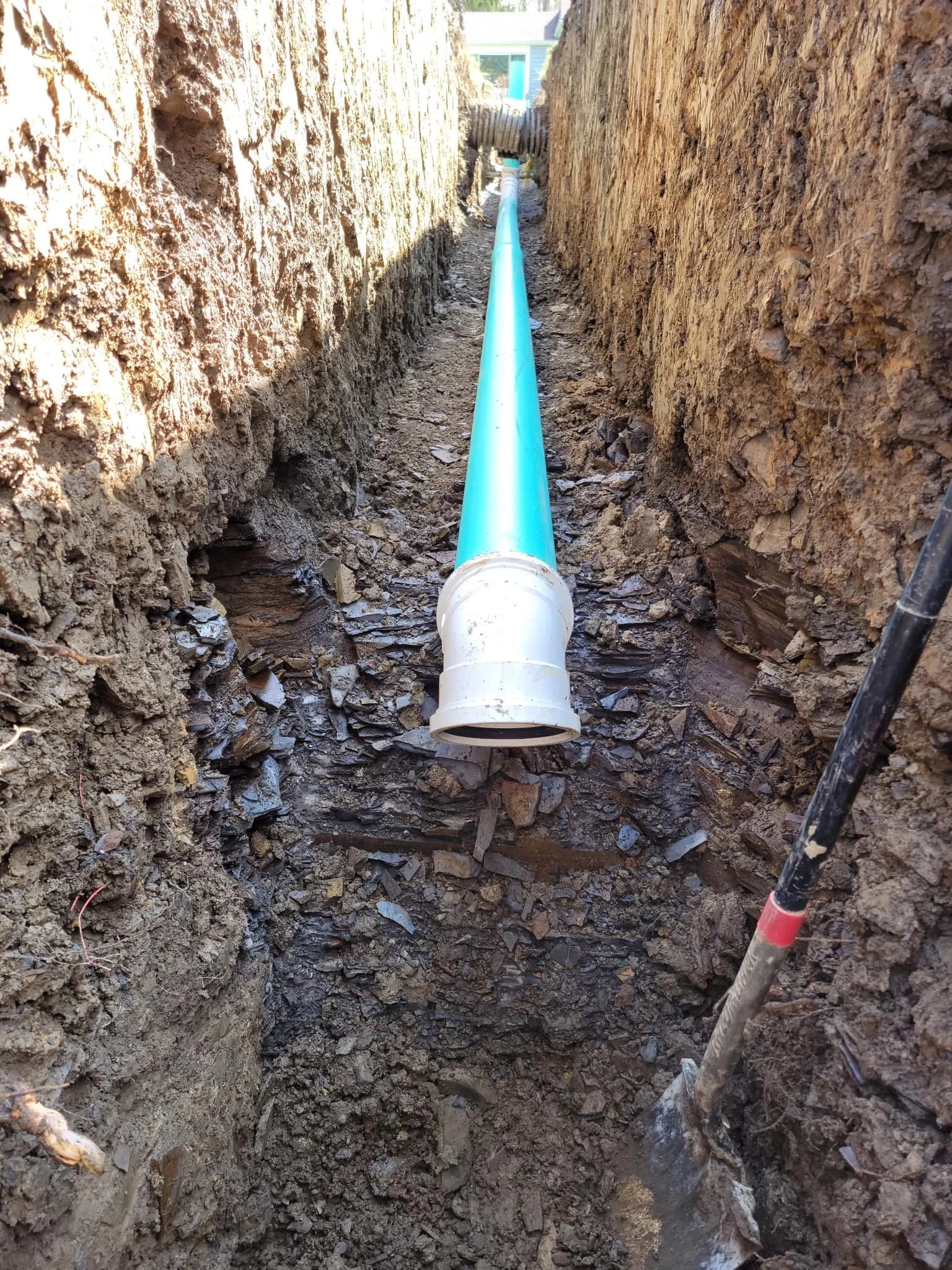 New PVC sewer pipe with cleanout in deep Buffalo yard trench with shovel