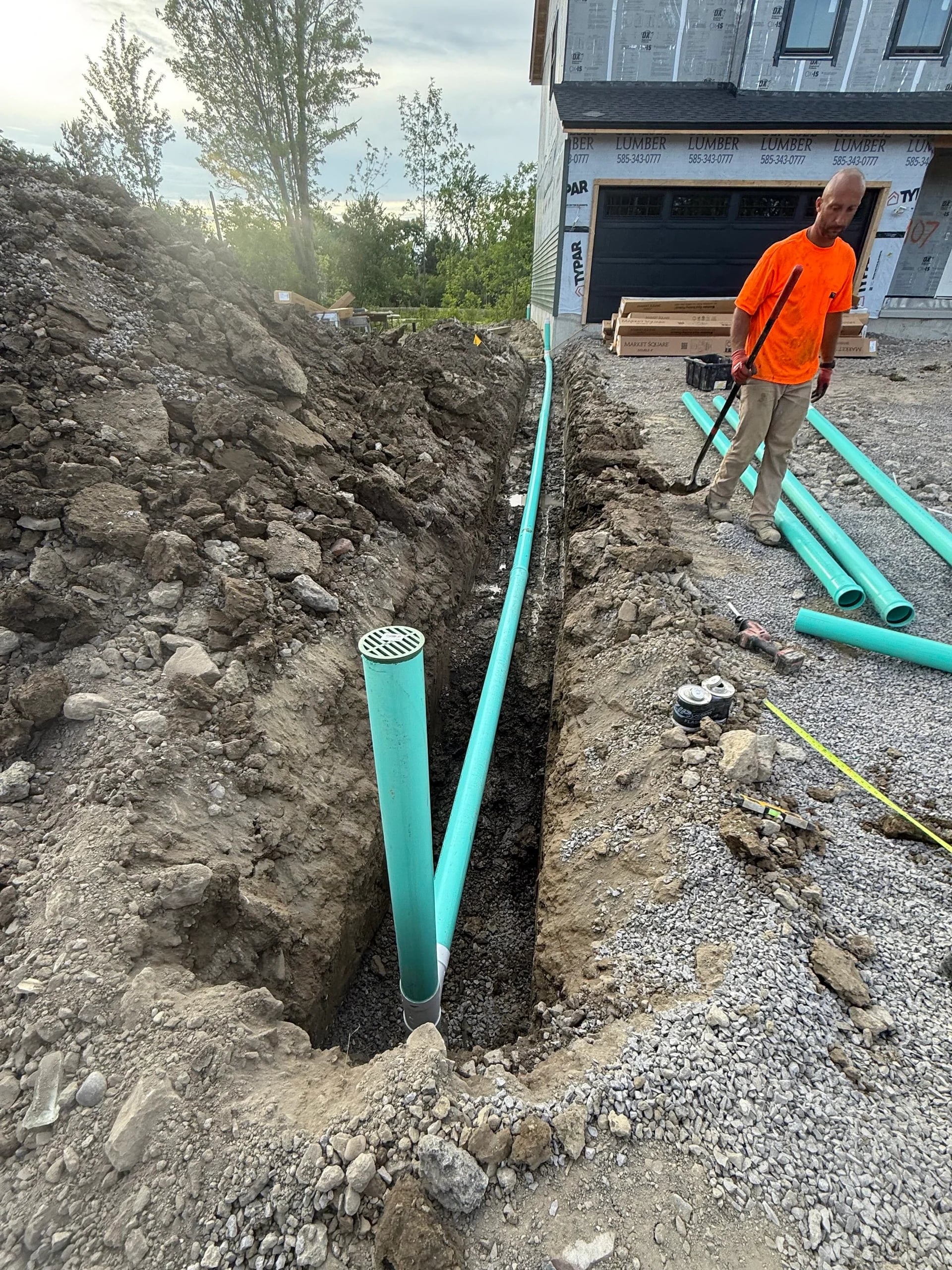 Worker in hi-vis installing drain grate and PVC pipes at new construction in Erie County