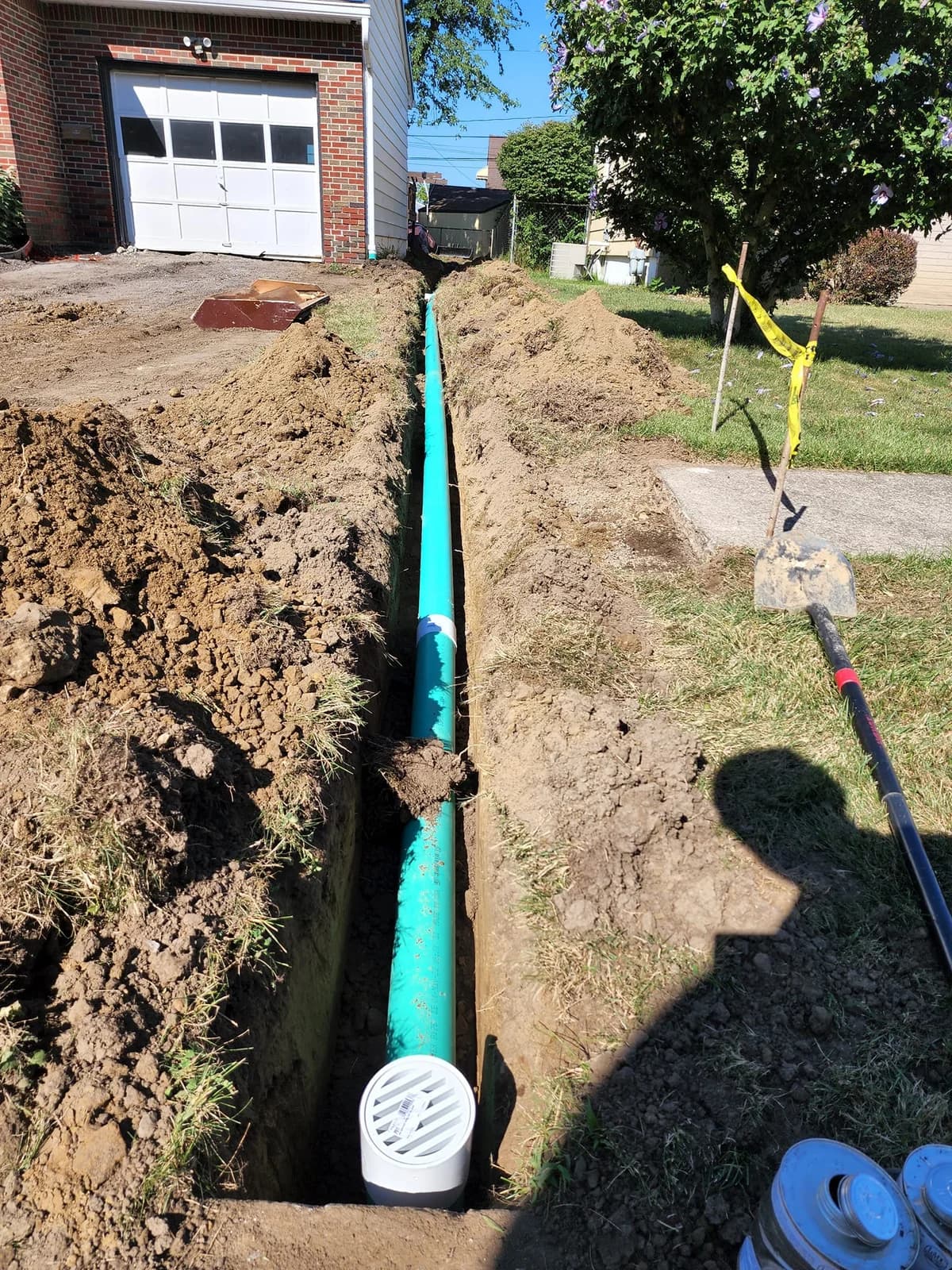 Green PVC sewer drain in Buffalo front yard trench from garage to sidewalk